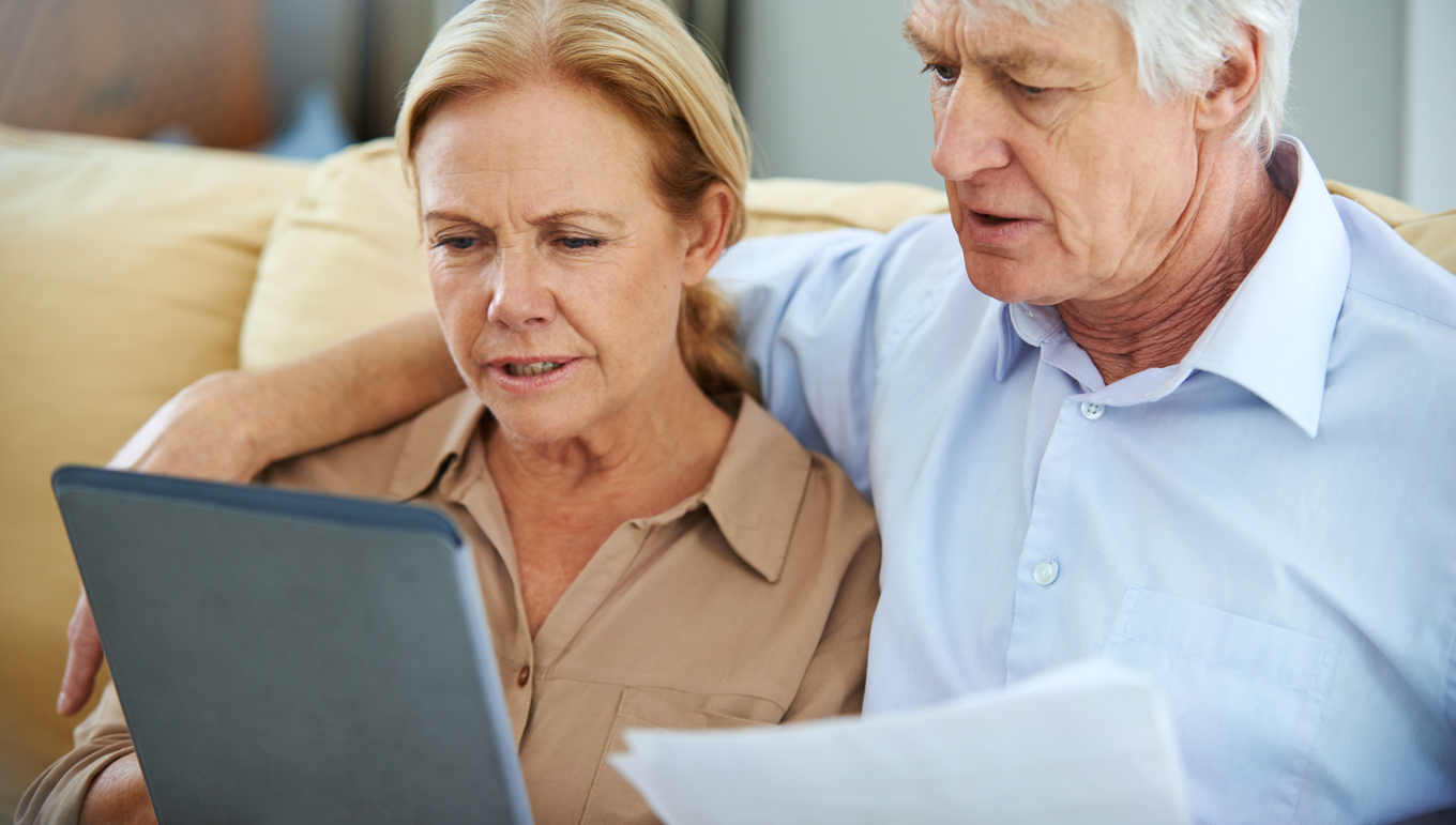 Elderly couple reviews paperwork on their tablet.