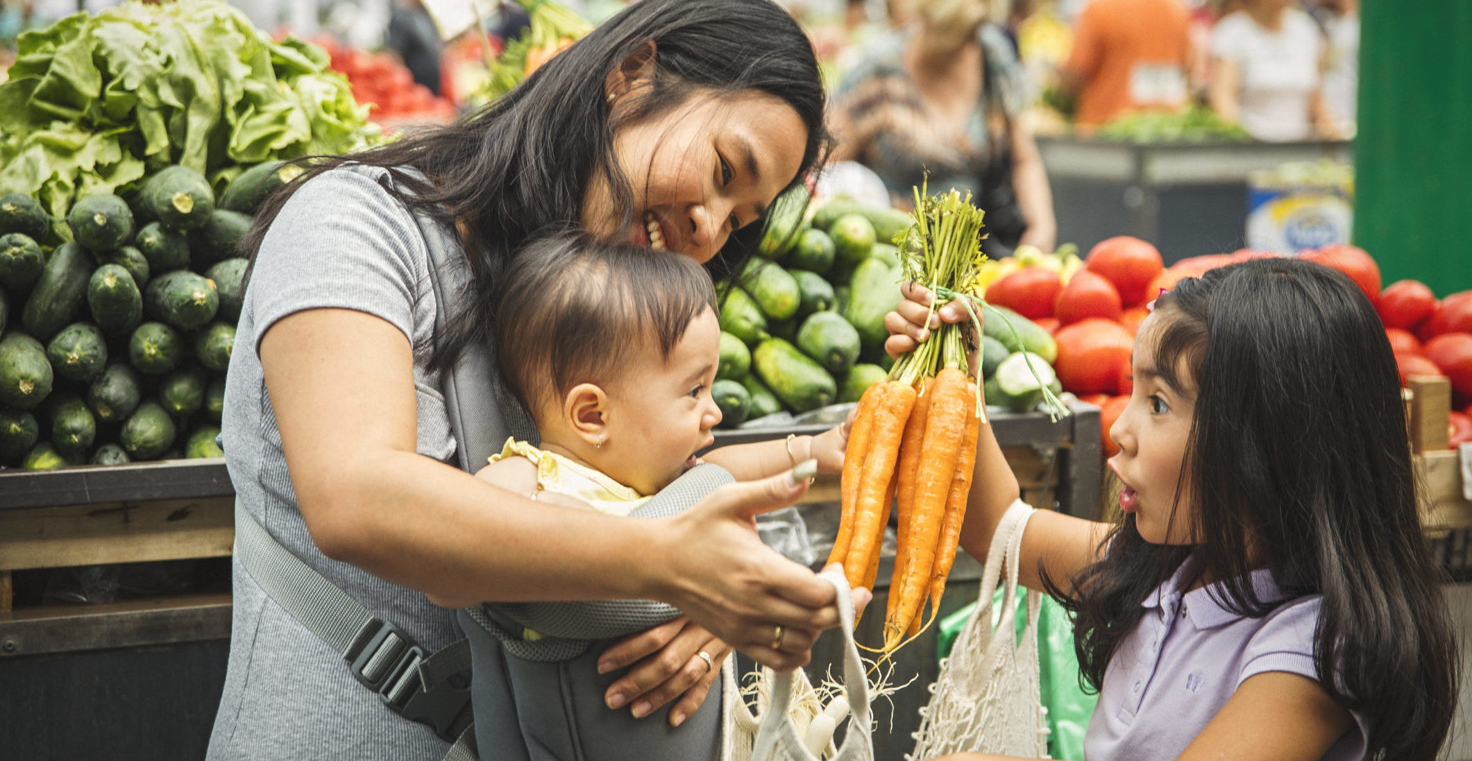 A mother and her two children shop for vegetables at a healthy food market.