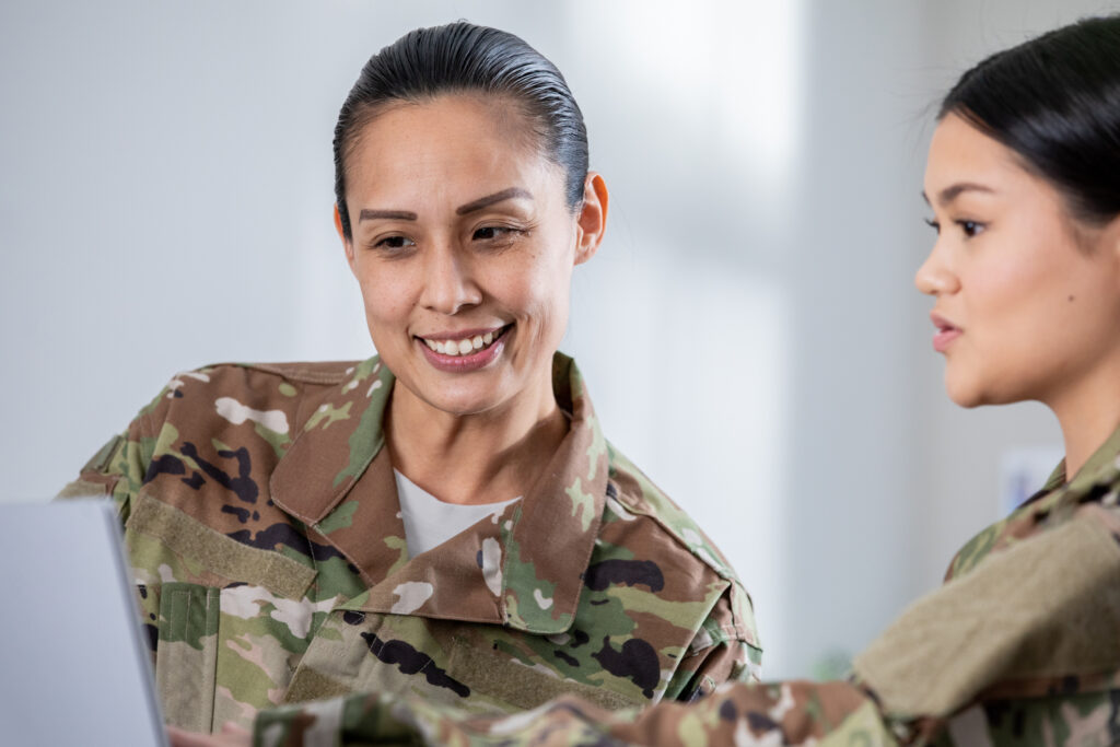 Two female veterans with medium skin tones discussing at a laptop.